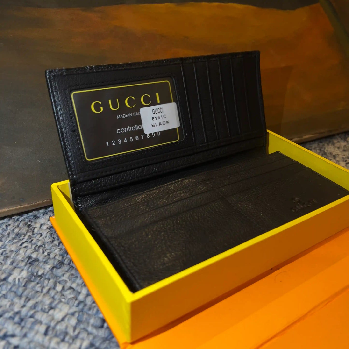 Black Gucci wallet in an open yellow box on a textured surface.